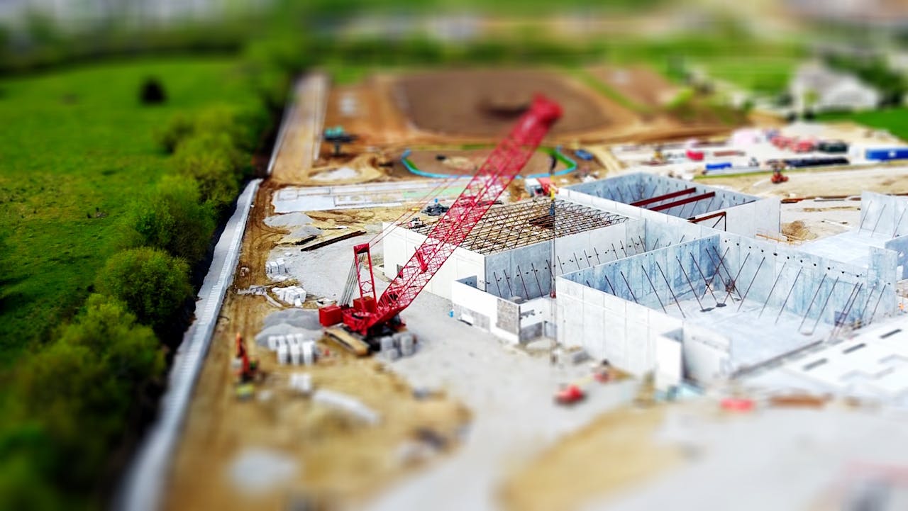 services-02 Aerial view of a construction site with a red crane amidst green fields and concrete buildings.